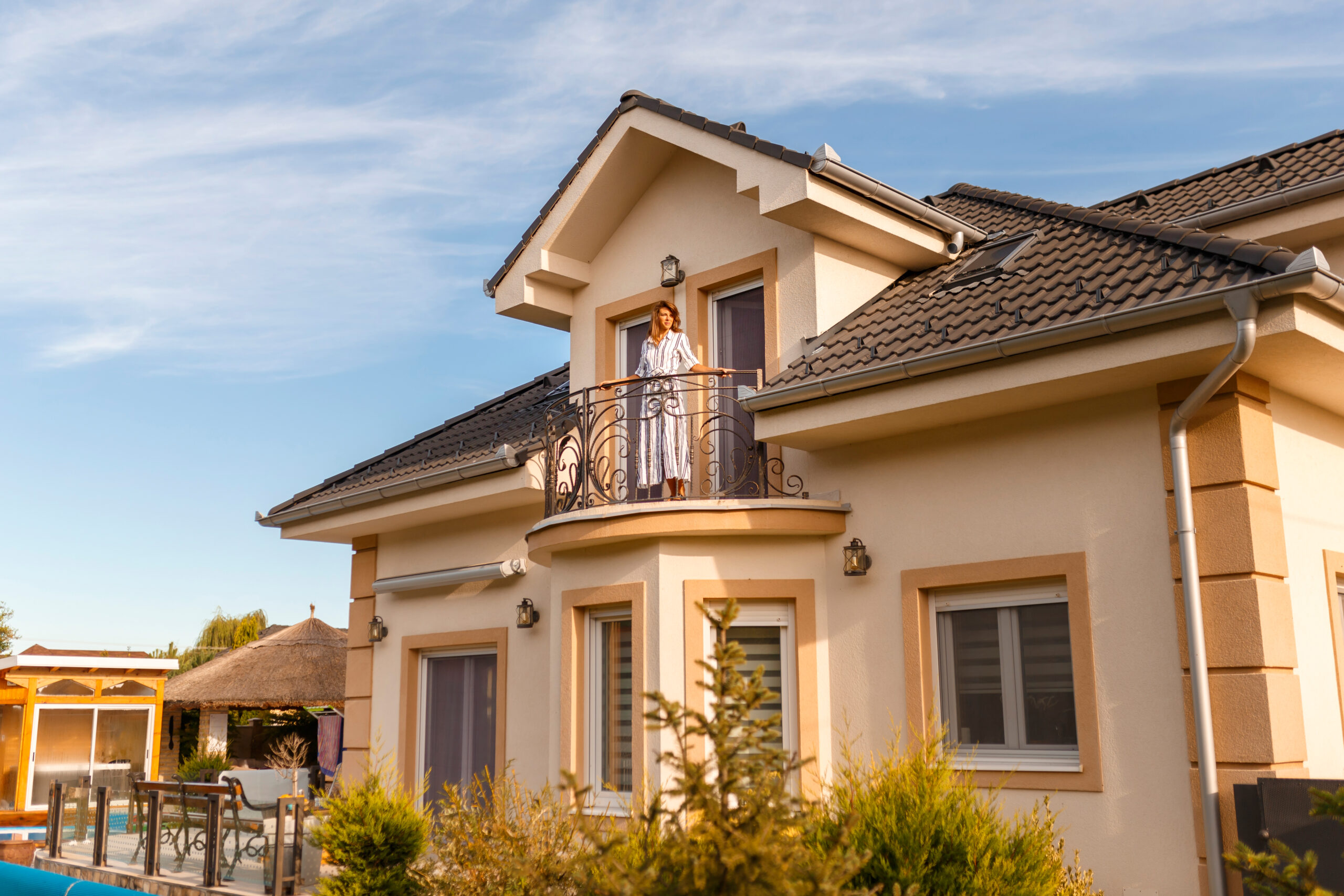 Beautiful young woman standing on her new house balcony happy after purchasing new property